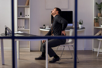 Young businessman suffering from back pain at table in office