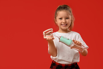 Cute little girl with oral irrigator and jaw model on red background