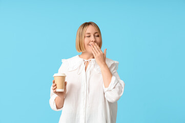 Tired adult woman with paper cup of coffee on blue background