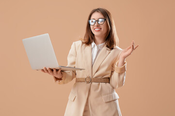 Pretty businesswoman in eyeglasses with laptop on beige background