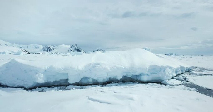 Massive snow covered iceberg in frozen ocean. Ice piece from crashed glacier towering Arctic coastline. Mountain range in background. Antarctica travel and exploration. Discover beauty of South Pole
