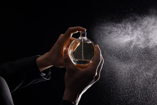 Young man spraying perfume on black background. Closeup