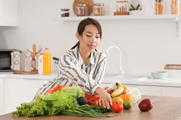 Young Asian woman taking tomato from counter in kitchen