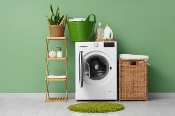 Modern washing machine with rack, baskets and detergents near green wall