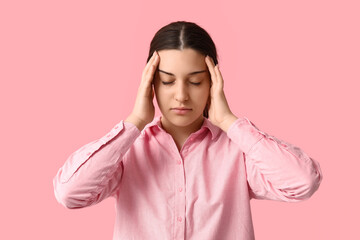 Beautiful young woman suffering from headache on pink background