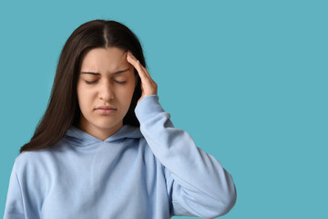 Beautiful young woman suffering from headache on blue background