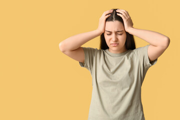 Beautiful young woman suffering from headache on yellow background