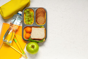 Lunch box with grape, cookies, bottle of water and stationery on white background. Top view