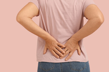 Mature woman suffering from back pain on pink background. Back view