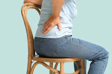 Mature woman suffering from back pain while sitting on chair on blue background