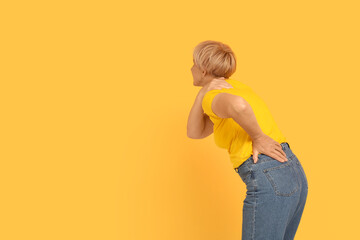 Mature woman suffering from back pain on orange background