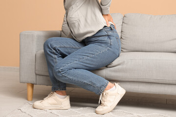 Mature woman suffering from back pain while sitting on sofa in living room