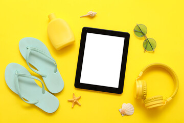 Tablet and beach accessories with flip-flops and headphones on yellow background. Top view