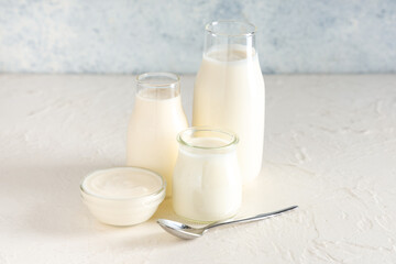 Bottles and glass bowl of tasty yogurt on white background