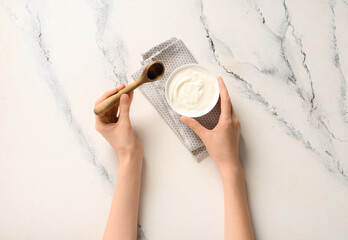 Female hands with bowl of tasty yogurt and wooden spoon on white background