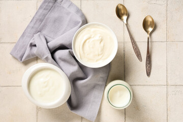 Bowls and bottle of tasty yogurt on white tile background