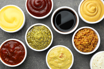 Many different sauces in bowls on grey table, top view