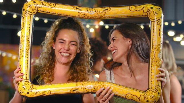 Female friends having fun posing with photo booth photo frame at party in bar - shot in slow motion