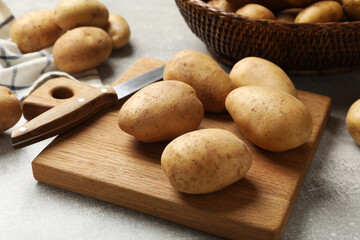 Many fresh potatoes, board and knife on grey table, closeup