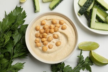 Tasty hummus with chickpeas in bowl and fresh products on light table, flat lay