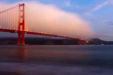 A cloud hovers over the Golden Gate Bridge in San Francisco during sunrise.