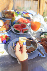 Hand spreading butter on Fresh homemade bread on full breakfast table background. Healthy eating and traditional bakery.