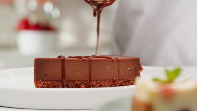 Pastry chef adding liquid chocolate topping on chocolate dessert cheesecake close-up. Cheesecake is a dessert made with a soft fresh cheese , typically cottage cheese, cream cheese, quark or ricotta