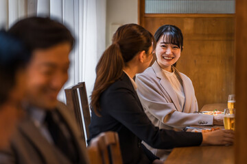 居酒屋・飲み屋のカウンターで部下と楽しくお酒を飲むビジネスウーマン
