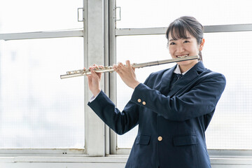 教室でフルートを吹く吹奏楽部のアジア人女子高生  © buritora