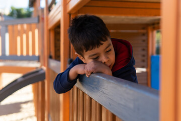 A thoughtful child sitting on playground equipment under the bright sun during daytime