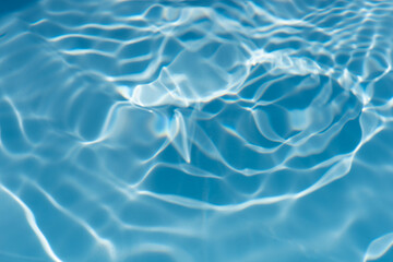 Blue water with ripples on the surface. Defocus blurred transparent blue colored clear calm water surface texture with splashes and bubbles. Water waves with shining pattern texture background.