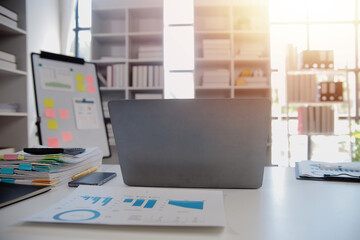 Close up view of simple workspace with laptop, notebooks, coffee cup and tree pot on white table with blurred office room background