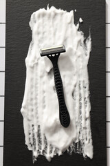 Shaving foam and disposable men's razor on black background, top view
