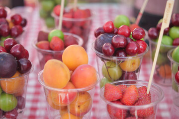 A colorful assortment of fresh mixed fruits served in cups on a checkered tablecloth