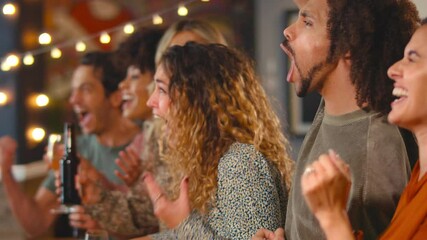 Group of multi-cultural friends celebrating watching sports game or match drinking in bar together - shot in slow motion
