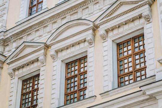 Four wooden windows on the facade of a house with beige plaster in the central historical part of the city. Beautiful decorative architecture with reliefs, cornice and white columns in Lviv, Ukraine.