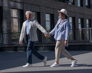 Obraz premium Stylish mature couple. Gray-haired man and woman holding hands while walking around the city. 