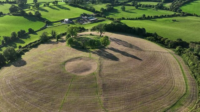 The Navan Fort, County Armagh, Northern Ireland, September 2022. Drone rises and pushes in to establish secluded tree grove on top of circular hilltop cultural heritage site.