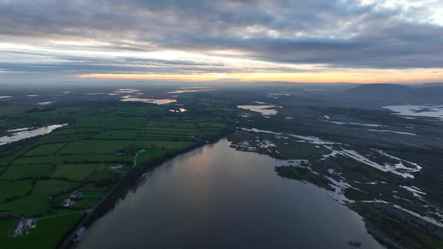 Lough Bunny, County Clare, Ireland, November 2023. Drone wide angle overview rises above lake separating farmland fields from floodplains at sunset dusk with blue hour spreading across landscape.