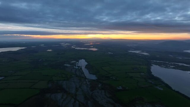 Lough Bunny, County Clare, Ireland, November 2023. Drone overview of stone walls cutting across the burren with orange yellow glow of light on horizon.