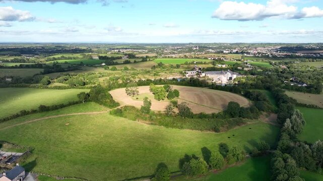 The Navan Fort, County Armagh, Northern Ireland, September 2022. Drone panoramic overview of circular hilltop with forested bank around edge with cloud shadows across top.