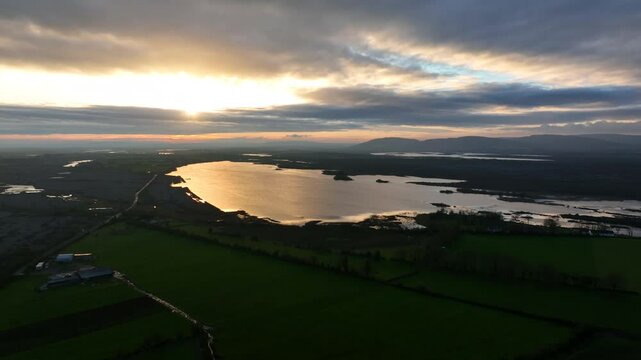 Lough Bunny, County Clare, Ireland, November 2023. Drone pans left orbiting lake in the Burren at sunset as brilliant rays of light reflect on water.