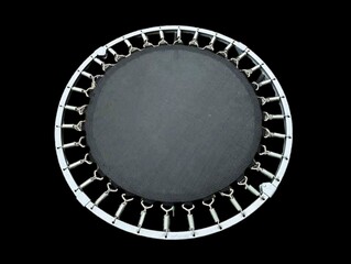 In the picture is a small black children's trampoline with a white steel wire border tied around a black circle. It is used for children's exercise. Jumping and playing helps keep them healthy.