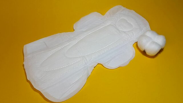 Sanitary napkin and cotton plant flowers. A concept that shows softness for the feminine area, is able to accommodate large amounts of blood and still keeps the feminine area dry, isolated on yellow.