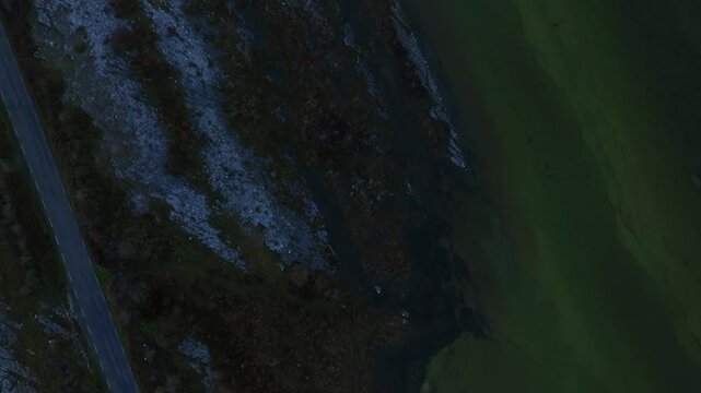 Lough Bunny, County Clare, Ireland, November 2023. Drone top down textured pattern of the burren landscape as cars drive by along road separating lake from land.