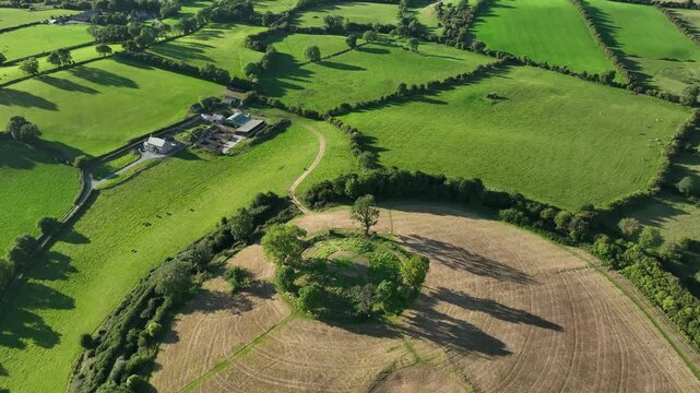The Navan Fort, County Armagh, Northern Ireland, September 2022. Drone high angle orbit left around hill surrounded by lush green fields on a beautiful sunny day.