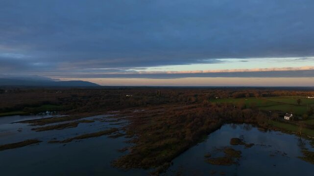Lough Bunny, County Clare, Ireland, November 2023. Drone dolly above flooded lakeshore edge with tufts of grass chunks sticking out of water at dusk.