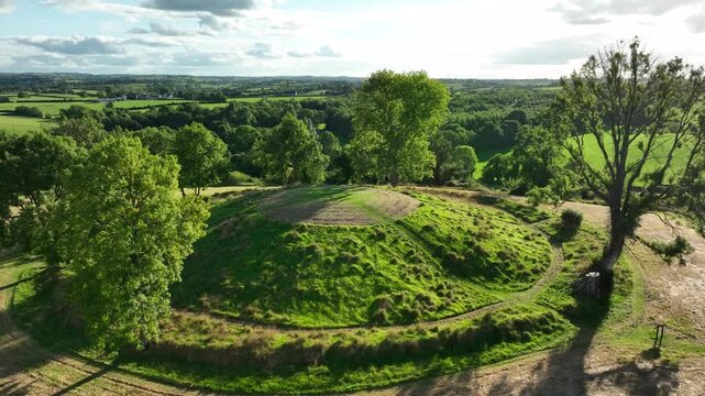 The Navan Fort, County Armagh, Northern Ireland, September 2022. Drone slowly orbits and rises above cultural heritage site on top of circular grassy hilltop to bird's eye top down view.