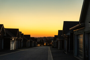 Obraz premium Sunset sky above suburban street - row of houses with prominent garages - warm golden hour light casting long shadows - clear, cloudless horizon - tranquil residential scene. Taken in Toronto, Canada.