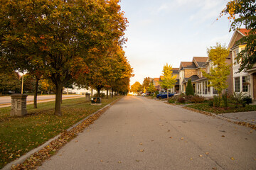 Autumn-draped suburban street at sunset - golden light filtering through changing leaves - tranquil neighborhood setting with lined residential homes. Taken in Toronto, Canada.